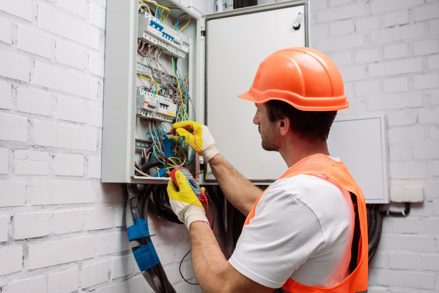 handsome-electrician-in-hardhat-and-gloves-holding-multimeter-near-electrical-distribution-box-e1669620094628